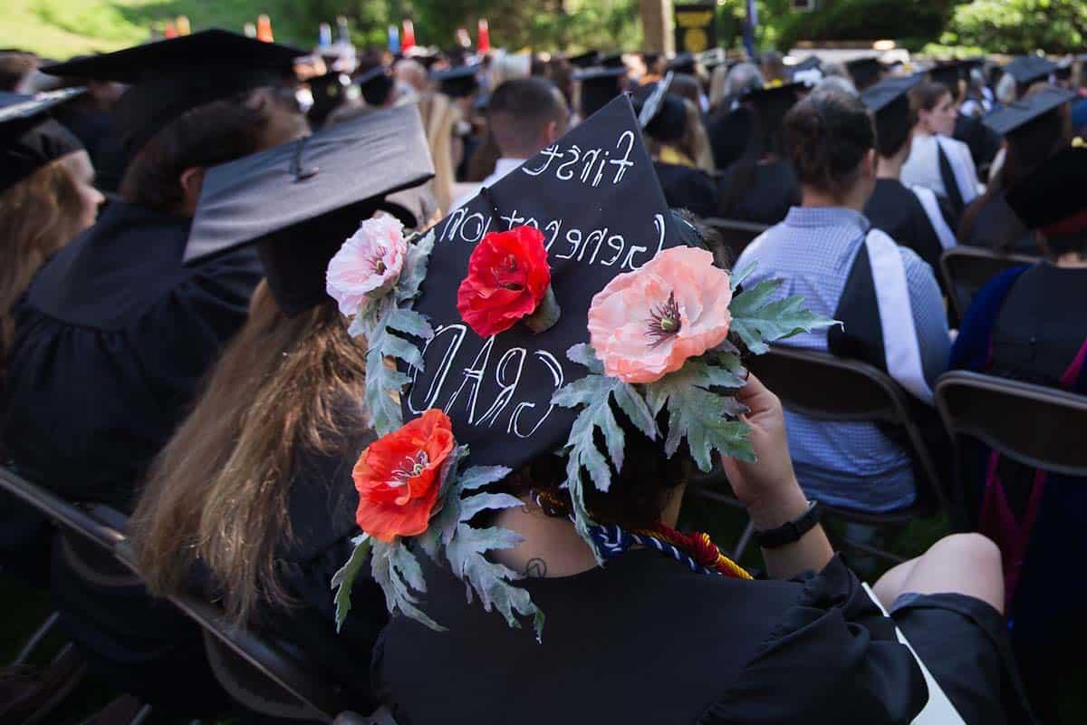 一名毕业生戴着一顶饰有鲜花和“第一代毕业生”字样的帽子.