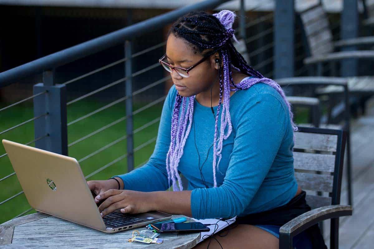 女学生在学生中心外的露台上用她的wi-fi连接的笔记本电脑工作.